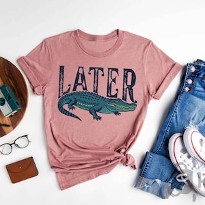 a pink shirt that says later next to a pair of jeans and a pair of