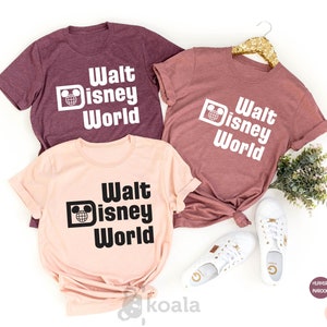 May include: Three t-shirts with the text "Walt Disney World" in a retro font. The shirts are in heather maroon, heather peach, and heather pink.