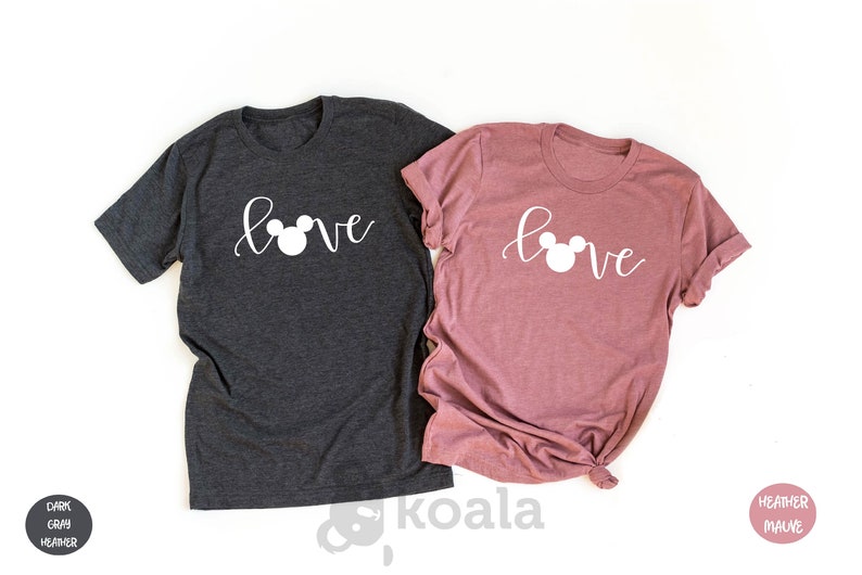 May include: Two t-shirts with the word "love" written in cursive with a Mickey Mouse head replacing the "o". The shirt on the left is dark heather grey and the shirt on the right is heather mauve.