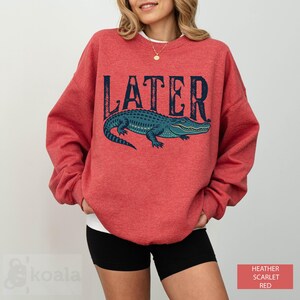 a woman wearing a red sweater with an alligator on it