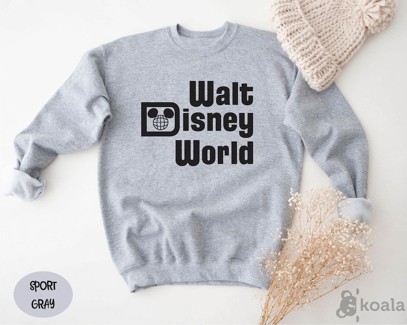 May include: A light gray sweatshirt with the words "Walt Disney World" in bold black letters. The design includes the iconic Mickey Mouse head and a globe. A light gray oval with the words "Sport Gray" is in the lower left corner.