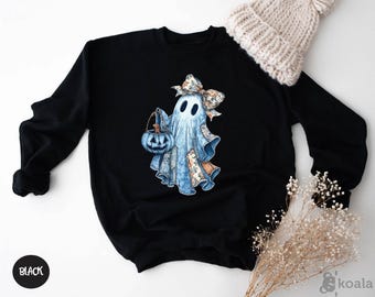 May include: Black sweatshirt featuring a watercolor ghost design holding a blue pumpkin bucket. The ghost has a floral bow and patchwork details. The word "BLACK" is printed on a black circle in the lower left corner.