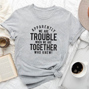 May include: A light gray t-shirt with black text that reads "Apparently we are trouble when we are together who knew!"