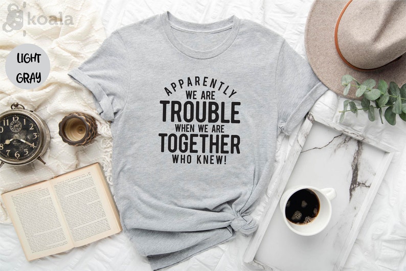 May include: A light gray t-shirt with black text that reads "Apparently we are trouble when we are together who knew!"