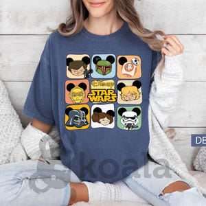 May include: A denim blue t-shirt featuring a grid of Star Wars characters with Mickey Mouse ears. The shirt includes images of Darth Vader, Boba Fett, and Luke Skywalker. The Disney Star Wars logo is also visible.