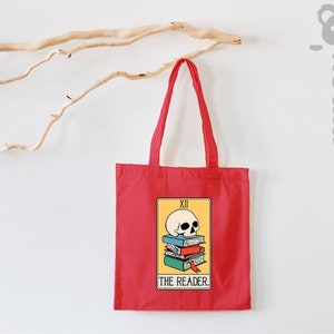 May include: Red tote bag with a yellow tarot card design featuring a skull on top of a stack of books. The card reads "XII THE READER."