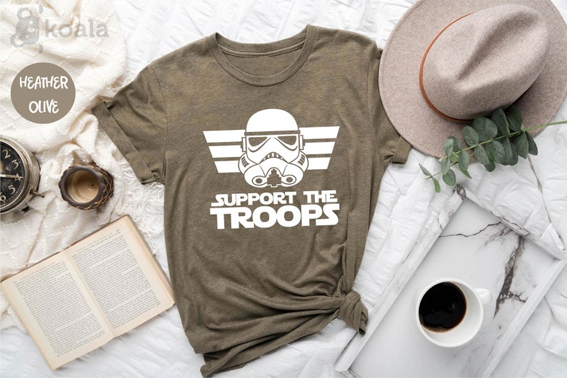 Peut inclure: Un t-shirt en olive chin&eacute; avec un graphique blanc d'un casque de Stormtrooper de Star Wars avec des ailes et le texte "Support the Troops".