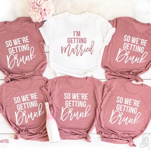 May include: Six t-shirts with different text printed on them. The shirts are a light pink color and the text is white. The text on the shirts reads "So we're getting drunk" and "I'm getting married".