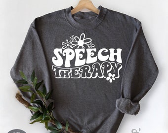 May include: Dark heather grey sweatshirt with white text that reads "Speech Therapy" in a retro font with white daisy flowers above and below the text.