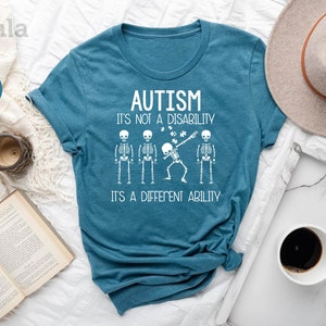 May include: A teal blue t-shirt with a white graphic of skeletons and the text "Autism It's not a disability It's a different ability".