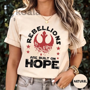 May include: A beige t-shirt with a black and red rebel alliance symbol and the text "Rebellions are built on hope".
