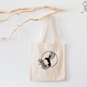 May include: A white tote bag with a black silhouette of a hummingbird with flowers in a circle design.