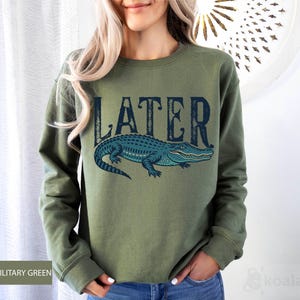 a woman wearing a green sweater with a blue alligator on it