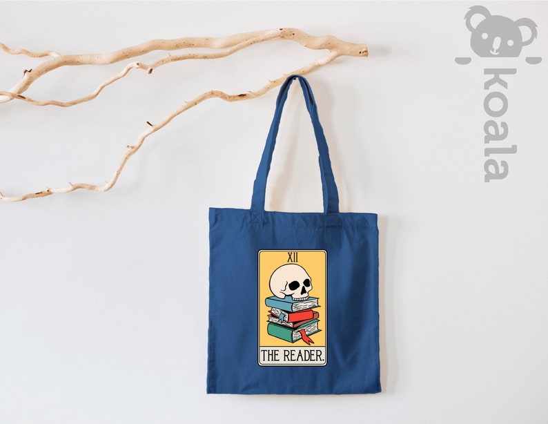 May include: A blue tote bag with a tarot card design featuring a skull on top of a stack of books. The card reads "XII THE READER."
