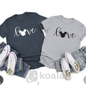 May include: Two t-shirts with the word "love" written in cursive with a Mickey Mouse head replacing the "o". One shirt is dark heather gray and the other is light gray.