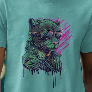 May include: A teal t-shirt featuring a graphic of a panther wearing sunglasses and a jacket. The panther illustration is in shades of green and black, with pink and yellow accents. The shirt is made of a soft material.