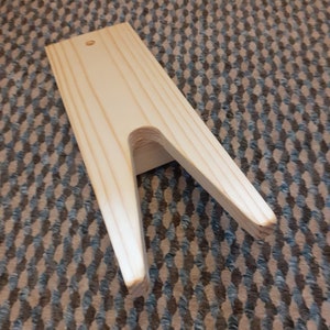 May include: A wooden shoe stretcher with a V-shaped opening. The stretcher is made of light brown wood and has a smooth finish.