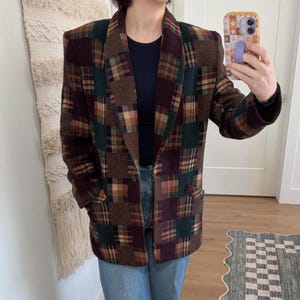May include: A vintage patchwork blazer in shades of brown, green, and burgundy. The blazer features a classic notched collar, two front pockets, and a single-button closure. The jacket is worn with a black top and blue jeans.