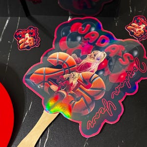 May include: A holographic basketball-themed cake topper with the text "Jada's 25th Year" in red script. The topper features a basketball player and basketballs. Additional stickers with text are also visible.