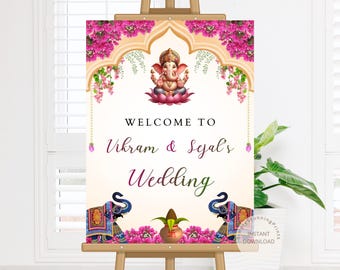 May include: A wedding welcome sign on an easel. The sign features a central image of the Hindu deity Ganesha, surrounded by pink floral accents. The text reads "Welcome to Vikram & Sejal's Wedding."