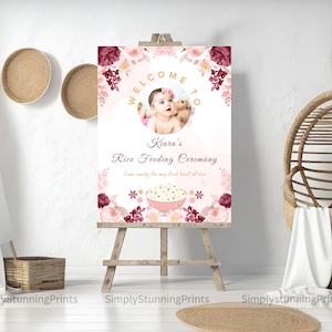 Pode incluir: Um cartaz de boas-vindas rosa e branco com detalhes florais e uma foto de uma menina pequena. O cartaz diz "Bem-vindo &agrave; Cerim&ocirc;nia de Alimenta&ccedil;&atilde;o de Arroz da Kiara. Estou pronta para minha primeira tigela de arroz."