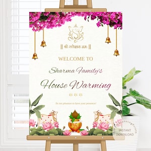 May include: A welcome sign for a housewarming event, displayed on an easel. The sign features floral and religious imagery, including a Ganesha illustration, bells, and lotus flowers. The text reads "Welcome to Sharma Family's House Warming."