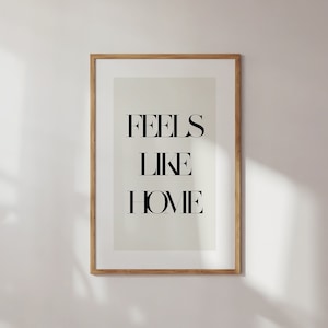 May include: A framed print with the text "FEELS LIKE HOME" in black lettering on a light beige background.