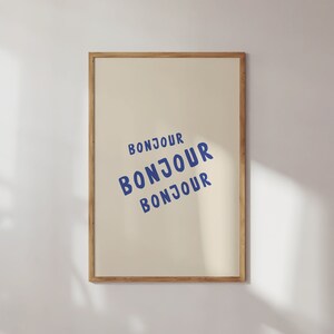 May include: A framed print with the word "Bonjour" repeated three times in a blue font on a cream background.