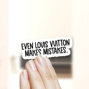May include: White sticker with black text that reads "Even Louis Vuitton makes mistakes."