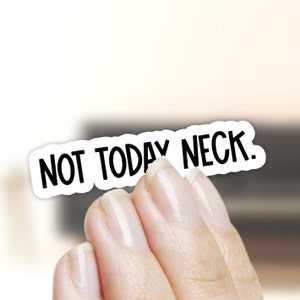 May include: A white sticker with the text "NOT TODAY NECK" in black, held by a hand. The sticker has a rounded rectangular shape and a white border. The background is blurred, with neutral tones.