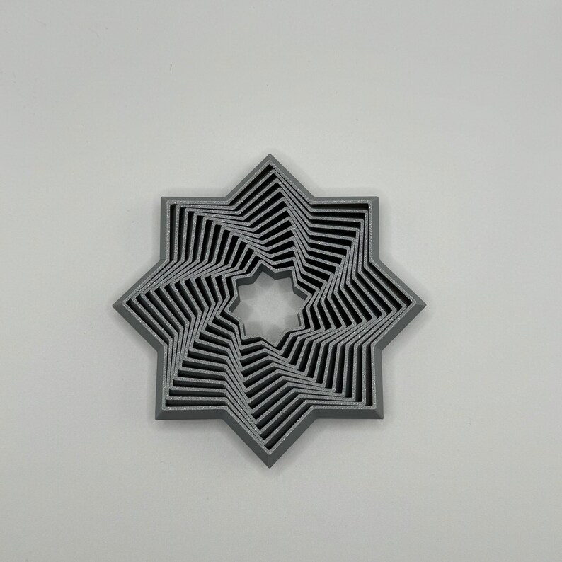 May include: A silver-colored, 3D printed, eight-pointed star with a layered design. The star has a central hole and is made of multiple layers of overlapping points.
