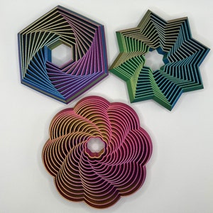May include: Three decorative metal wall hangings in the shape of a star, a flower, and a hexagon. The star is green and blue, the flower is pink and gold, and the hexagon is purple and blue.