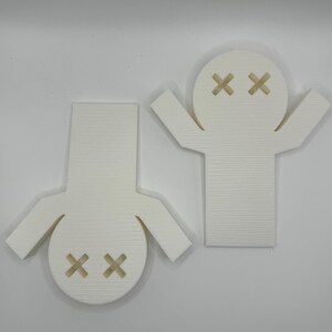 May include: Two white 3D printed figures with a simple design. Each figure has a round head with two black X's for eyes. One figure has arms raised above its head, while the other figure has arms at its sides.