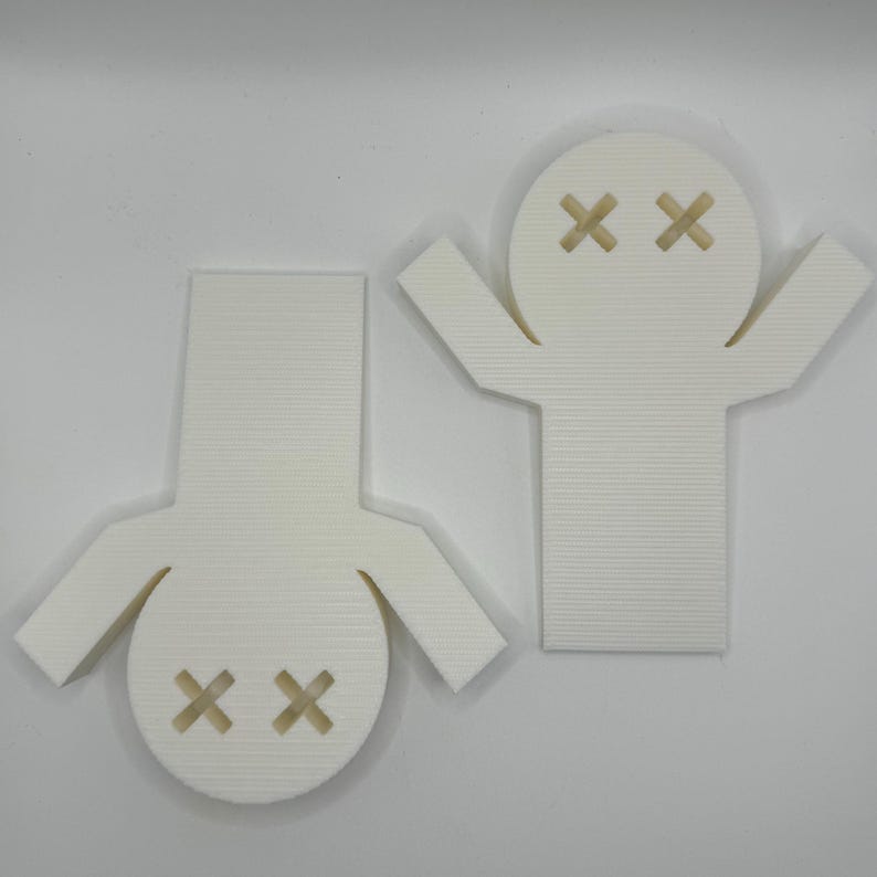 May include: Two white 3D printed figures with a simple design. Each figure has a round head with two black X's for eyes. One figure has arms raised above its head, while the other figure has arms at its sides.