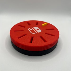 May include: A red and black circular game cartridge storage case with a Nintendo Switch logo and a yellow tab.