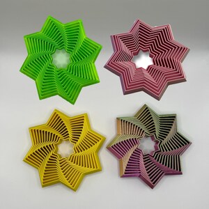 May include: Four decorative star-shaped coasters in different colors: green, pink, yellow, and purple. Each coaster has a spiral design with a central hole.