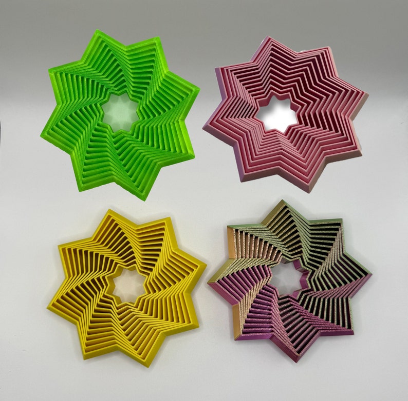 May include: Four decorative star-shaped coasters in different colors: green, pink, yellow, and purple. Each coaster has a spiral design with a central hole.