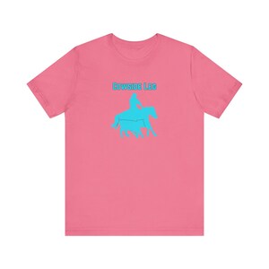 May include: Pink t-shirt with a blue silhouette of a person riding a horse and the text "COWSIDE LEG" in blue.
