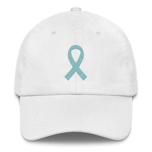 May include: White baseball cap with a curved peak. The cap has a light blue ribbon embroidered on the front. The ribbon has a striped pattern. The cap is made of a soft fabric and has a classic, casual style.