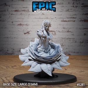 May include: A gray, detailed miniature sculpture of a woman sitting inside a large, open rose. The woman is wearing a flowing robe and has long hair. The base of the sculpture is a large, round, black base. The sculpture is 51mm in size. #5281