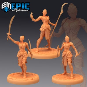 May include: Three miniature figures of a female humanoid with reptilian features. The figures are painted in a light brown color and are posed in different stances. One figure is holding a sword, another is holding a staff, and the third is holding two daggers.