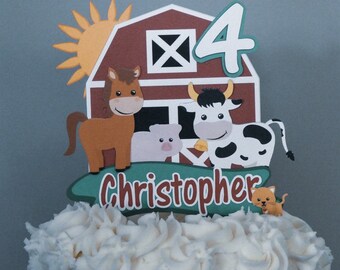 Puede incluir: Un adorno para pastel de granero rojo con un caballo, una vaca, un cerdo y un gato. El granero tiene una X blanca en el frente y el número 4 en la parte superior. El adorno también incluye una pancarta verde con el nombre Christopher.