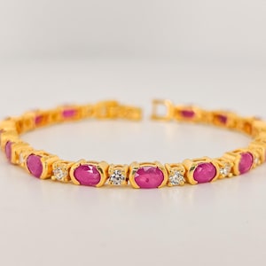 May include: A gold bracelet with oval, vivid pink gemstones and small, clear accent stones. The bracelet has a delicate chain and a clasp. The jewellery piece is a classic and elegant design, suitable for various occasions.