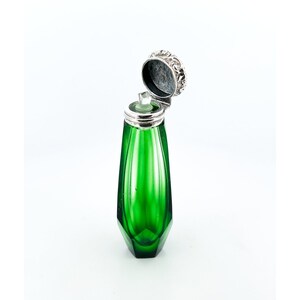 Puede incluir: Una botella de vidrio verde con una tapa de plata. La botella tiene forma de diamante y un diseño facetado. La tapa está abierta y la botella está vacía.