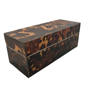 May include: A rectangular box with a tortoiseshell pattern. The box is primarily brown with darker brown and tan markings. The lid fits snugly on the base, creating a clean, seamless look. The box is likely used for storage or display.