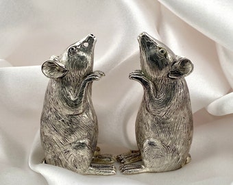 May include: A pair of silver mouse salt and pepper shakers. The mice are standing on their hind legs with their tails curled up. They have detailed features, including eyes, whiskers, and fur.