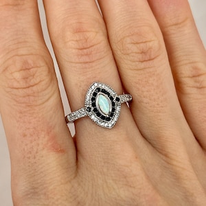 May include: A silver ring featuring a marquise-shaped opal stone set within a halo of smaller white and black stones.