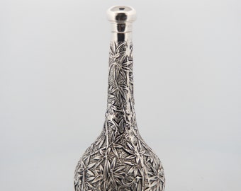 May include: A silver vase with an intricate floral design. The vase has a round base and a long, slender neck.