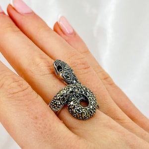 Op de afbeelding: Een zilveren ring met een gekruld slangontwerp met zwarte marcasietstenen.