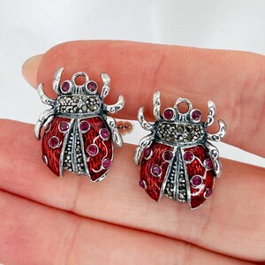 Puede incluir: Un par de pendientes de plata con forma de mariquita con esmalte rojo y detalles de marcasita.